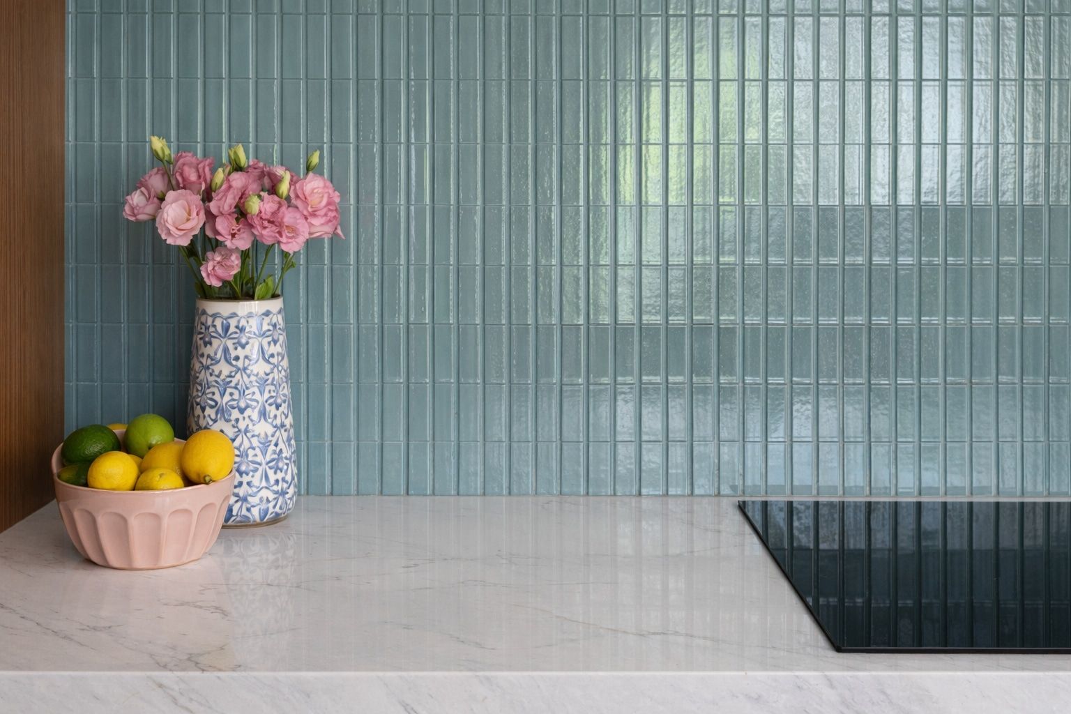 Sage green glass tile wall with a blue and white vase of pink flowers and a bowl of lemons