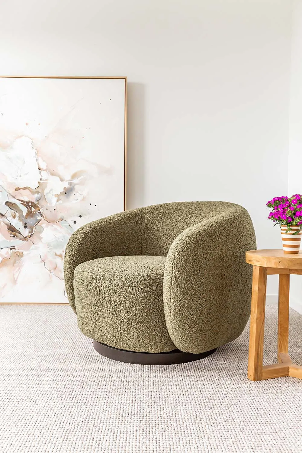 Bouclé tub chair beside a timber side table and abstract artwork in a bedroom