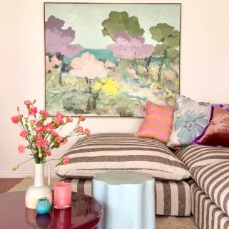 Striped daybed with cushions beneath a landscape artwork and pink flowers