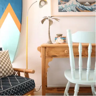 Timber desk with a pale blue spindle chair, lamp and surfboard artwork