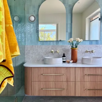 Blue tiled bathroom with a timber vanity, arched window and yellow towel