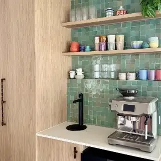 Coffee station with green tiles, open shelves of glassware and an espresso machine