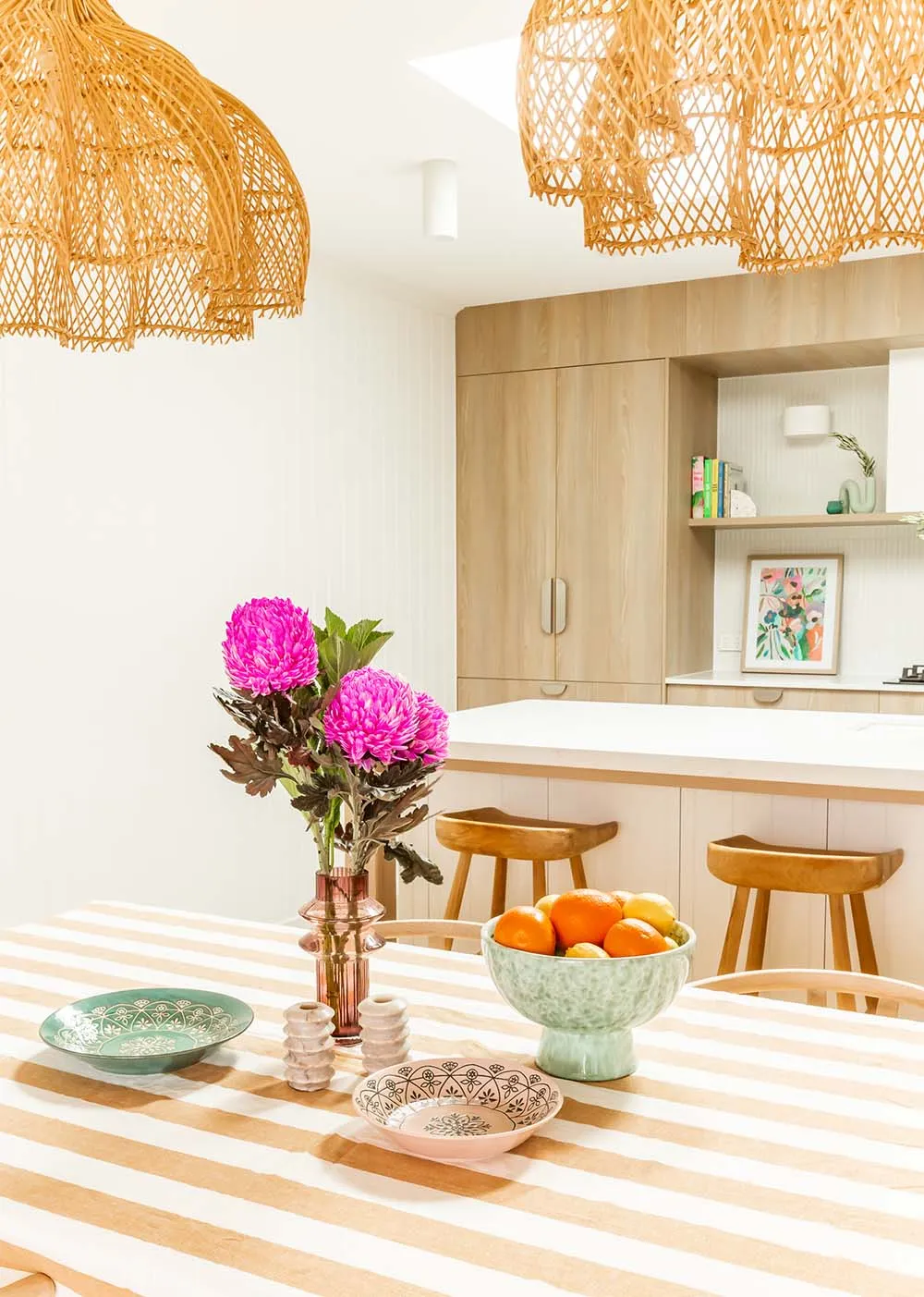 Kitchen with rattan pendants, pink flowers and a fruit bowl on a striped tablecloth