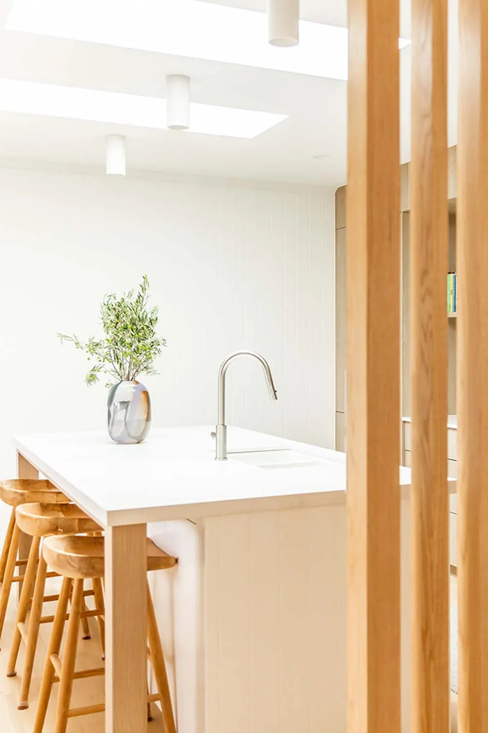 White kitchen island with timber stools behind a vertical timber batten screen