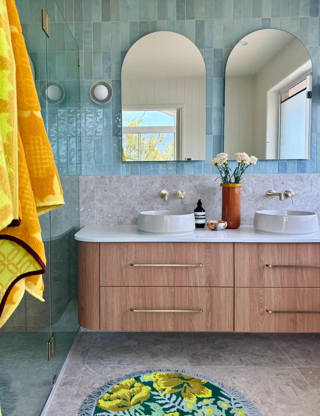 Ocean-blue tiled bathroom with twin arched mirrors and a timber vanity