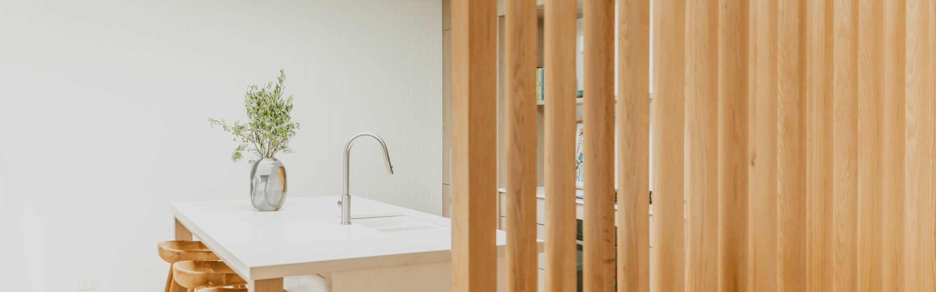 White kitchen island with a curved tap behind vertical timber battens