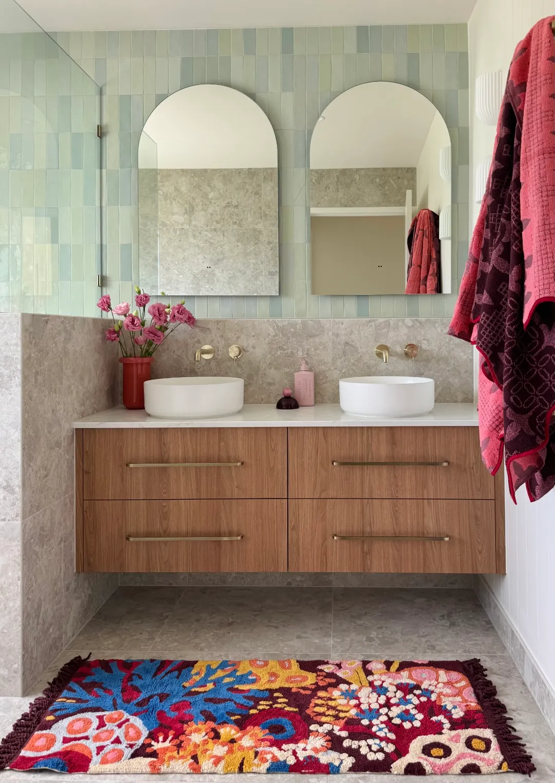 Double timber vanity with mint tiles, arched mirrors and a colourful floral rug