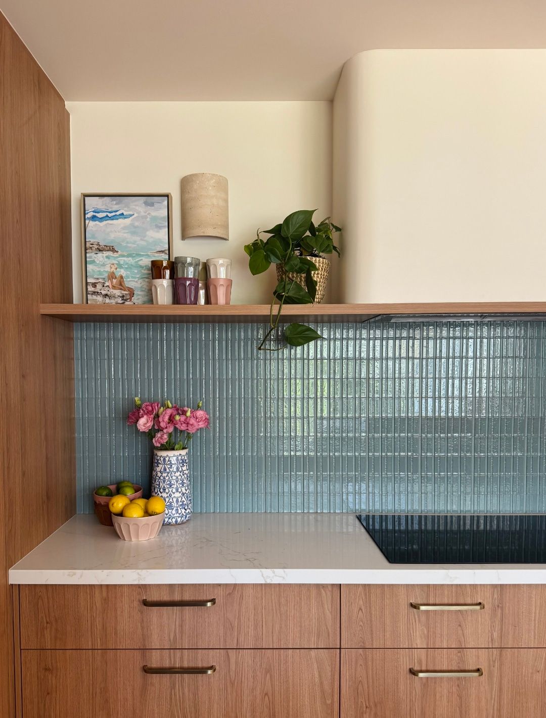 Kitchen nook with a sage glass tile splashback, timber shelf and pink flowers